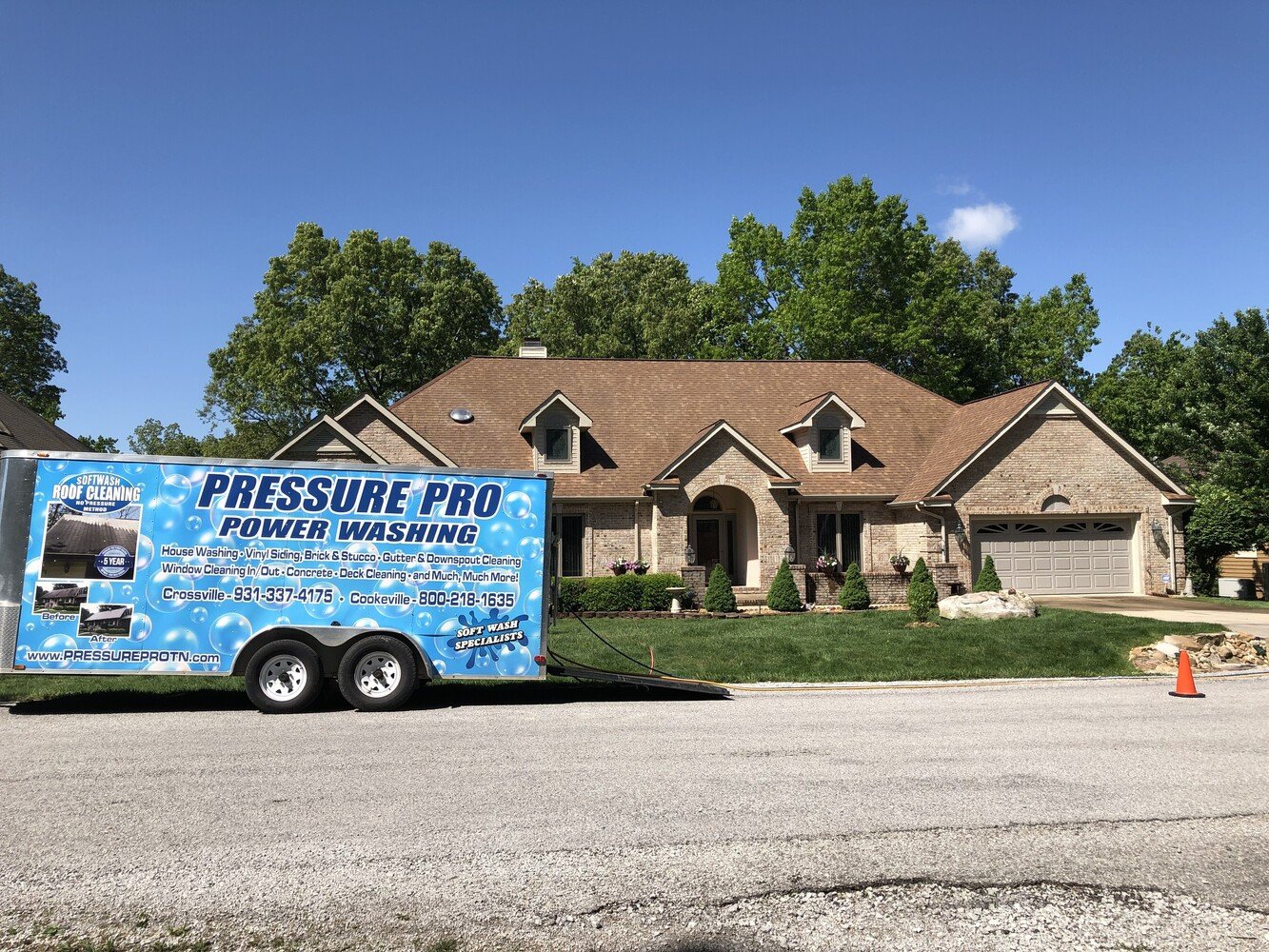 Pressure Pro Power Washing branded trailer in front of a freshly cleaned brick home